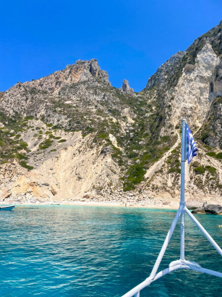 Am Bild sieht man der Bug eines kleinen Schiffs, der in die Richtung der felsigen Küste Korfu gerichtet ist.