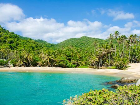 Man sieht einen Sandstrand vor dem türkisblauen Meer an der Küste des Nationalparks Tayrona in Kolumbien, einem der Ziel einer Wanderreise.