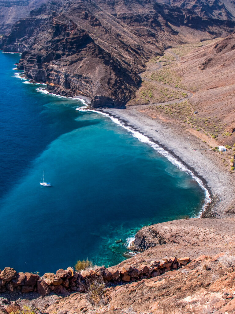 Der Playa de la Guancha ist am Bild von oben zu sehen. Der Strand liegt abgelegen auf La Gomera, in der Bucht vor dem Strand kann man ein kleines Segelboot erkennen, doch der Strand selbst ist menschenleer.