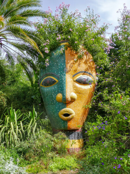 Eine Installation im ANIMA-Garten von Andre Heller in Marrakesch. Sie sieht aus wie eine große Maske mit offenem Mund umringt von Pflanzen, die dabei wirken wie die Haare der Maske.