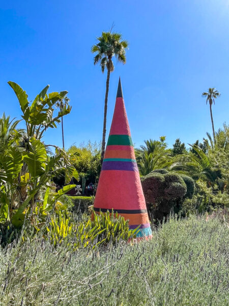 Eine kegelförmige Skulptur ragt im Garten von Andre Heller zwischen Gebüsch hervor.