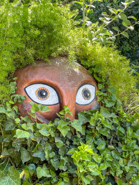 Man sieht eine Skulptur im Anima Garden in Marrakesche. Sie wirkt wie ein Gesicht, umringt von Pflanzen, das überrascht auf die Wanderreisenden blickt, die sich ihren Weg durch die Kunst-Installationen bahnen.