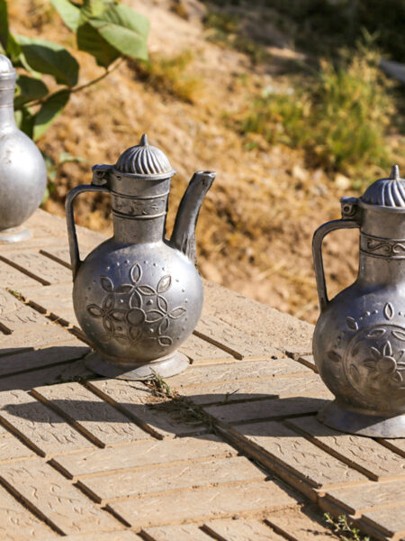 Mehrere traditionelle usbekische Teekannen stehen auf einer Holzplattform. Im Hintergrund kann man Teile der usbekischen Landschaft erkennen.