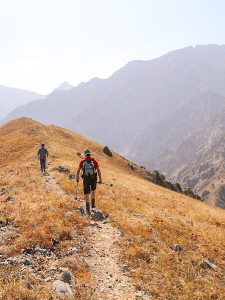 Zwei Personen wandern einen Berggrat in Usbekistan entlang. Im Hintergrund kann man die zentralasiatische Berglandschaft erkennen.