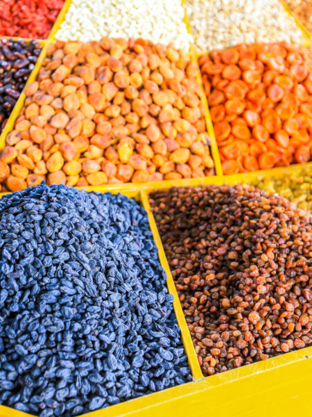 Diverse Gewürze und Hülsenfrüchte liegen auf einem gelben Marktstand in einem Basaar in Usbekistan.