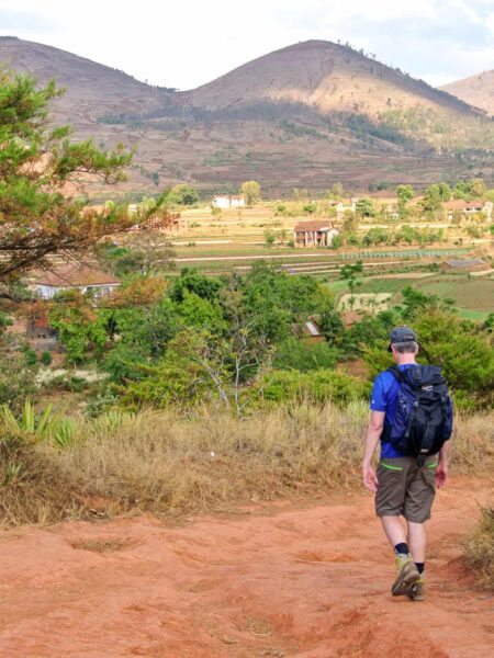 Ein Mann wandert einen Weg auf Madagaskar hinab. Über seine Schulter sieht man Teile des Hochlands von Madagaskar.