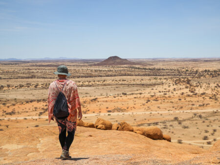 Allein wandernde Person blickt über eine weite, stille Wüstenlandschaft in Namibia.