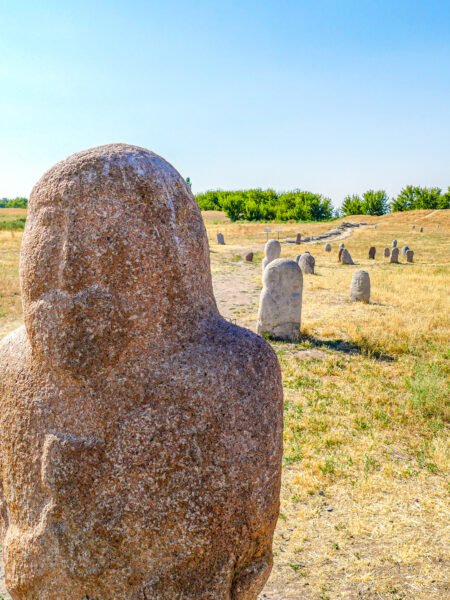 Man sieht eine kleine Statue in der Nähe des Burana-Turms in Kirgistan. Im Hintergrund kann man noch weiter dieser Statuen erkennen, die sich in der Steppe verlieren.