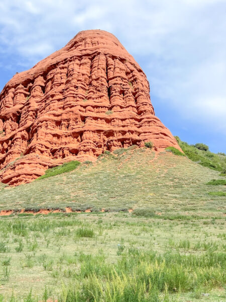 Man sieht ein Felsmassiv aus rotem Stein in Kirgistan. Im Vordergrand lassen sich die Steppen des Landes erkennen, während der Fels ein Ausläufer des Märchencanyons sein könnte.