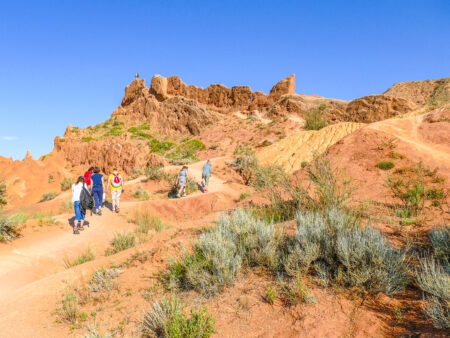 Mehrere Personen auf Wanderreise gehen einen Hang Zentralasien hinauf. Sie folgen dem Wanderweg durch den Märchencanyon.