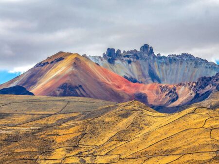 Ein Landschaftsfoto, das den Tunupa-Vulkan in Bolivien in der Ferne zeigt. Während die Wiese im Vordergrund gelb-grün in der Sonne strahlt, erscheint der Vulkan in der Ferne rötlich durch die Erde.