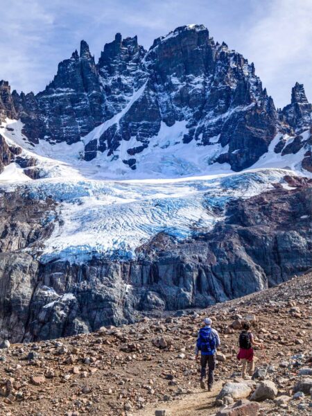 Zwei Personen wandern durch den Nationalpark Cerro Castillo in der Region Aysén. Sie befinden sich aktuell auf Wanderreise mit dem Reiseanbieter Weltweitwandern. Im Hintergrund ragt der namensgebende Cerro Castillo in den Himmel auf.