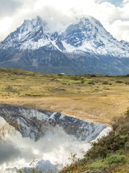 Ein Landschaftsfoto aus dem Nationalpark Torres del Paine in Patagonien. Im Hintergrund ragen zwei Gipfel in den Himmel auf, die sich am kleinen See im Vordergrund spiegeln.