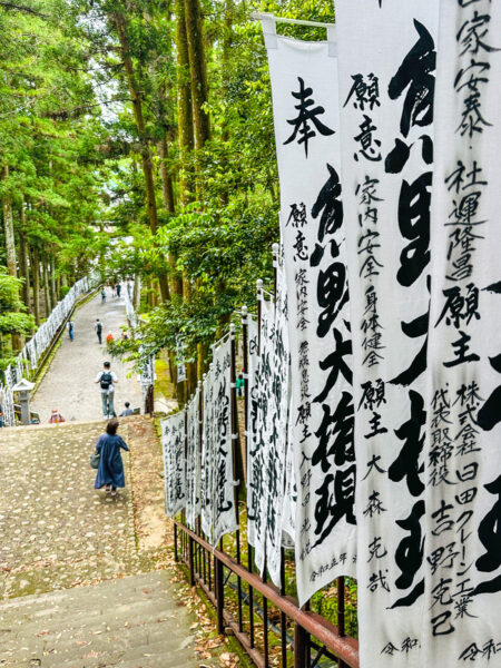 Flaggen mit japanischen Schriftzeichen stehen neben einer Treppe, die zum Schrein Kumano Hongu Schrein in Japan hinaufführt, einem der Highlights auf der Reise mit Weltweitwandern.