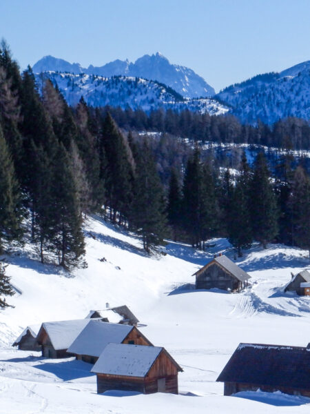 Das Ausblick über der Almhütte der Filzmoosalm auf das verschneite Gesäuse im Winter hinab. In der Ferne kann Teil des steirischen Berglands erkennen.