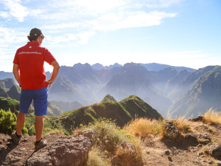 Ein Guide von Weltweitwandern in einem roten T-Shirt steht mit dem Rücken zur Kamera vor einem Aussichtspunkt in Madeira und schaut in ein Tal hinab.