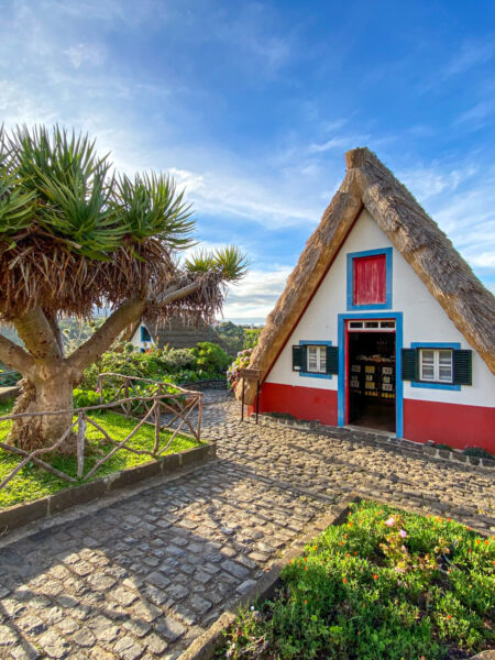 Eine der Casas Típicas de Santana auf der Insel Madeira vor einem blauen sommerlichen Himmel.