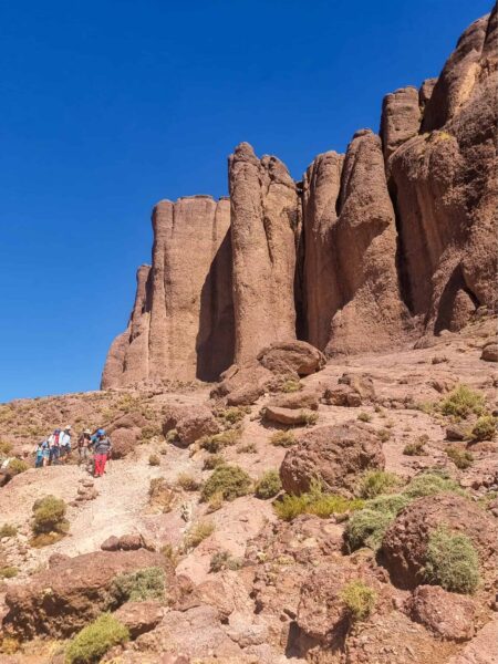 Eine kleine Gruppe auf einer Wanderreise mit dem Reiseanbieter Weltweitwandern folgt einem Pfad durch die Jbel Sarhro in Marokko. Rechts von ihnen türmen sich im Bild die hohen Felswände auf, für die das Gebirge gekannt ist.