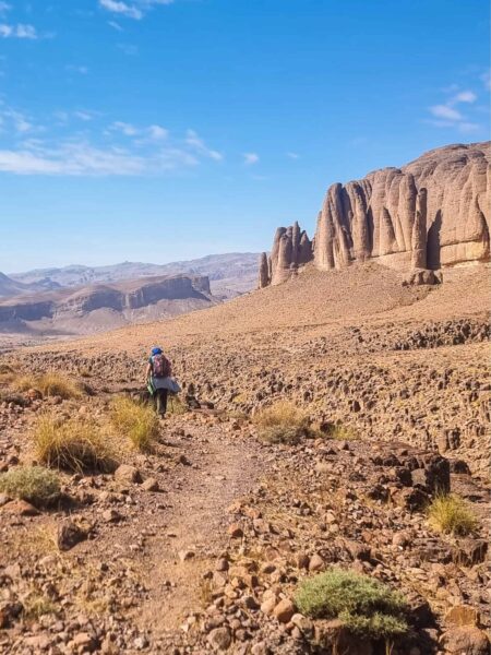 Eine Wanderin auf einer Trekkingreise durch das Jbel Sarhro folgt einem Pfad. Große Teile des Bilds werden eingenommen von dem strahlend blauen Himmel Marokkos.
