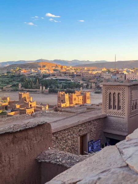 Man sieht auf dem Foto Aït Benhaddou, ein befestigtes Dorf (Ksar) in Marokko. Im Vordergrund kann man Teile der Mauern erkennen, während im Hintergrund die Landschaft des Hohen Atlas zu sehen ist.