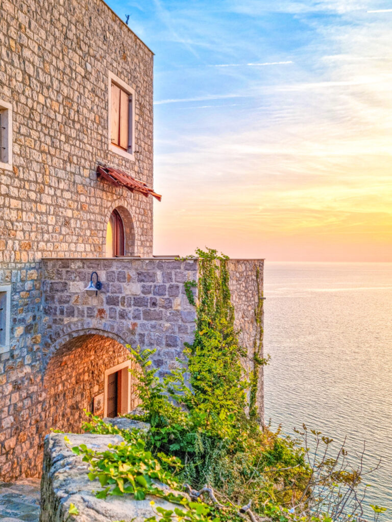 Man sieht ein Gebäude in der montenegrischen Festung Ulcinj im Licht der untergehenden Sonne. Im Hintergrund kann man die Adria erkennen und den orangen Schein des Sonnenuntergangs.