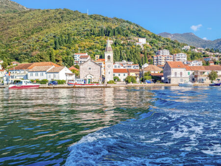Man sieht eine malerische Kleinstadt in der Bucht von Kotor in Montenergro vom Wasser aus. Das Foto wurde von einem Boot aus auf einer Bootstour im Zuge einer Wanderreise aufgenommen.