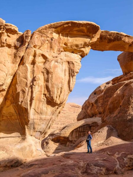 Ein Mann auf einer Trekkingreise durch Jordanien steht unter der Um Fruth Felsenbrücke in Wadi Rum.