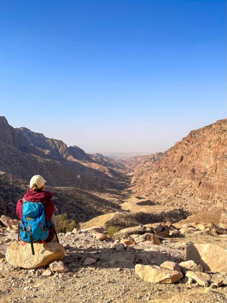 Eine Person auf einer Trekkingreise mit Weltweitwandern sitzt auf einem erhöhten Punkt im Dana Biosphärenreservat in Jordanien und genießt die Aussicht über das weite Tal, das sich vor ihr ausbreitet.
