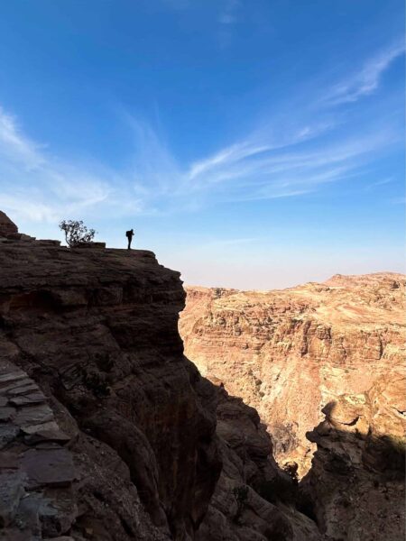 Eine Person auf einer Wanderreise steht an einem atemberaubenden Ausblick in Jordanien und schaut hinaus auf die karge Landschaft, die sich um sich herum ausbreitet.