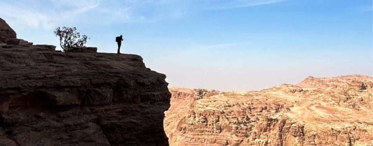Eine Person auf einer Wanderreise steht an einem atemberaubenden Ausblick in Jordanien und schaut hinaus auf die karge Landschaft, die sich um sich herum ausbreitet.