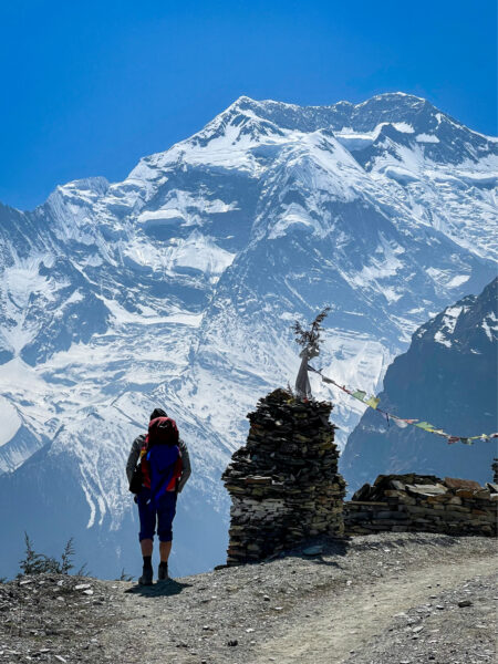 Ein Mann auf einer Trekkingreise in Nepal steht an einem Aussichtspunkt entlang des Annapurna-Circuit und schaut in die Berglandschaft hinaus, die ihn hier umgibt.