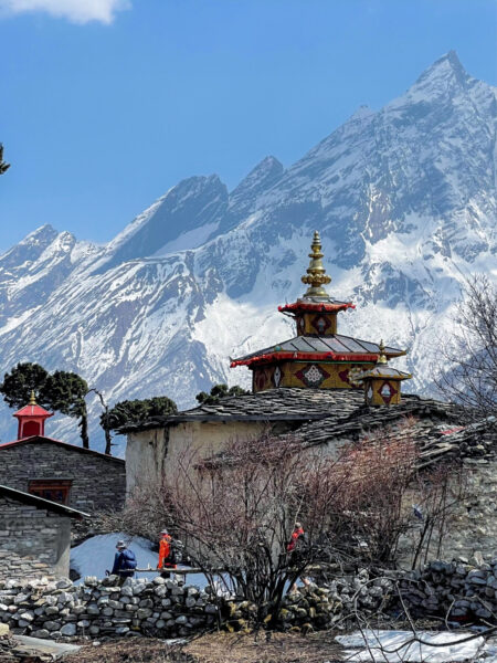 Ein nepalisches Bergdorf entlang der Manaslu-Umrundung. Im Hintergrund ragt der Manaslu-Gipfel in den Himmel auf.