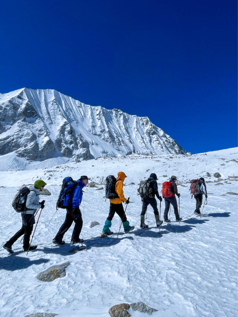 Eine kleine Gruppe auf Trekkingreise geht durch eine schneebedeckte Landschaft, im Zuge ihres Circuit-Trekks rund um den Manaslu.