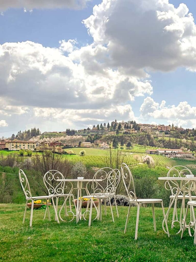 Mehrere Tische und Stühl stehen auf einer grünen Wiese vor den Hügel des Piemont. Sie sind leer, bieten aber genug Platz für die kleine Gruppe an Wander-Reisenden, die in die Region gekommen ist, um die Landschaft und die Kulinarik zu genießen.