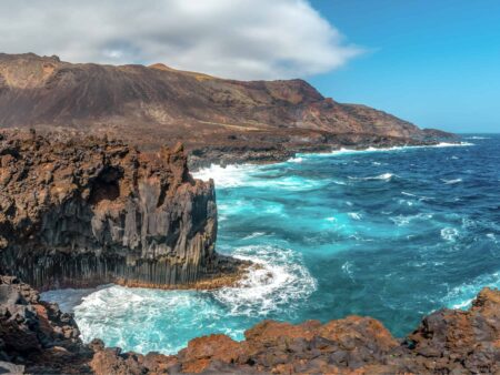 Man sieht die Vulkanlandschaft an der Küste von El Hiero, sowie den türkisblauen atlantischen Ozean, der an den zerklüfteten Klippen bricht.