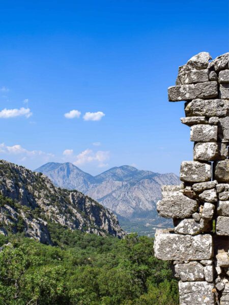 Ein Landschaftsfoto aufgenommen von den Ruinen von Termessos. Jenseits eines Mauernausschnitts kann man die Gebirgslandschaft der Türkei erkennen.