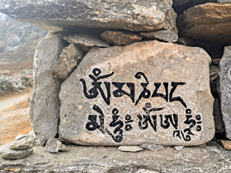 Tibetische Schrift wurde auf einen Stein gemalt. Sie stellt ein Gebet dar. Im Hintergrund sieht man ein wenig der Berglandschaft in Nepal.