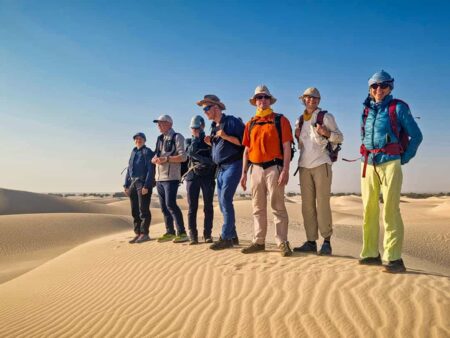 Eine kleine Wandergruppe steht gemeinsam auf einer Sanddüne im Oman. Hinter ihnen breitet sich die Wüste aus, die sie während ihrem Wanderurlaub besuchen.