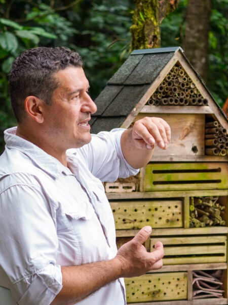 Ein Guide von Weltweitwandern erklärt der Reisegruppe etwas über einen ihrer Halte in Costa Rica. Er gestikuliert mit den Händen und hinter ihm kann man ein Insektenhotel ausmachen.