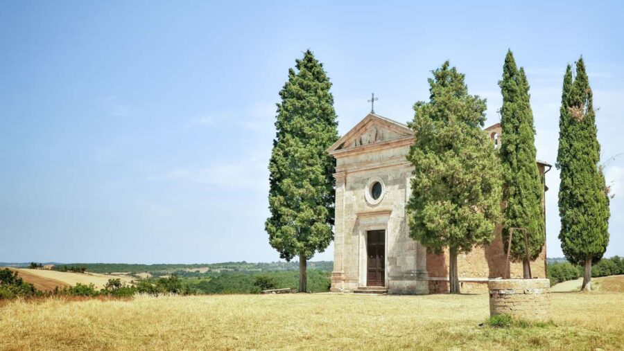 Toskan, Landschaft mit Gras, grünen Bäumen und einer Kirche, blauer Himmel im Hintergrund