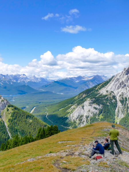 Drei Personen auf einer Wanderreise durch Kanada machen eine Pause mit einem Ausblick auf die kanadischen Rocky Mountains. Sie gehen gerade auf dem Sulphur Skyline Trail.