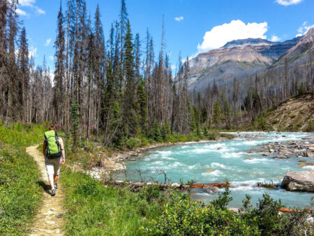 Ein Foto einer Wanderin, die einem Weg neben einem kanadischen Fluss entlanggeht.