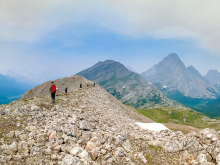 Mehrere Personen wandern einen Berggrat in den kanadischen Rockys entlang. Zu beiden Seiten des Berges sieht man die Tiefen Täler unter ihnen.