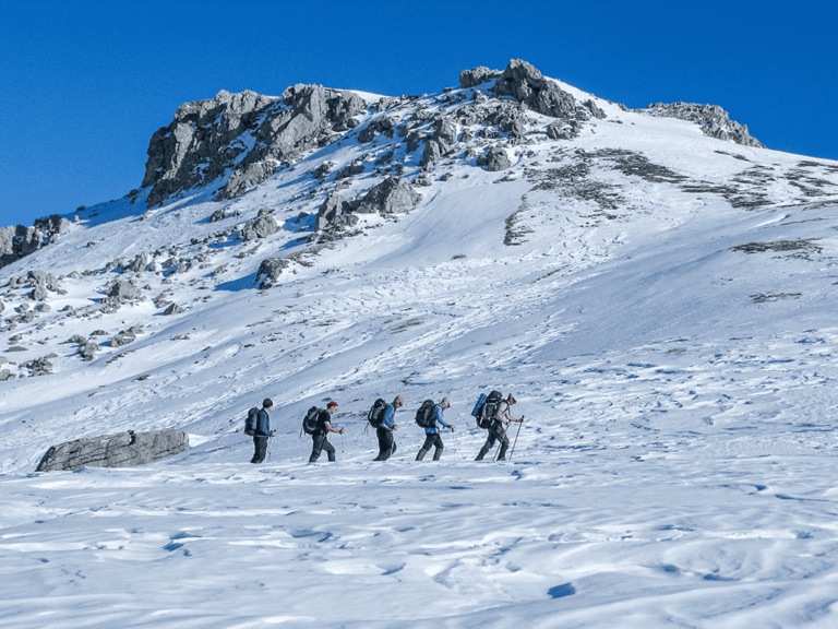 Kleine Wandergruppe mit Rucksäcken unterwegs in verschneiter Berglandschaft – geführtes Wintertrekking mit Weltweitwandern behauptet nachhaltiges Reisen und Naturerlebnis.