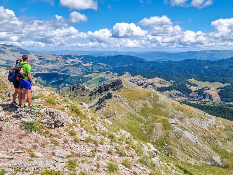 Zwei Wanderer mit Trekkingstöcken in grüner Karstlandschaft – achtsames Unterwegssein in der Natur auf einer nachhaltigen Wanderreise mit Weltweitwandern.
