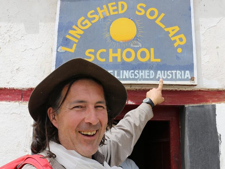 Christian Hlade zeigt auf das Schild der Lingshed Solar School in Ladakh. Das Foto symbolisiert nachhaltige Entwicklung, lokale Projekte und die Werte von Weltweitwandern