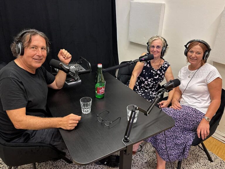 Christian, Greta und Petra sitzen an Mikrofonen in einem Podcast-Studio