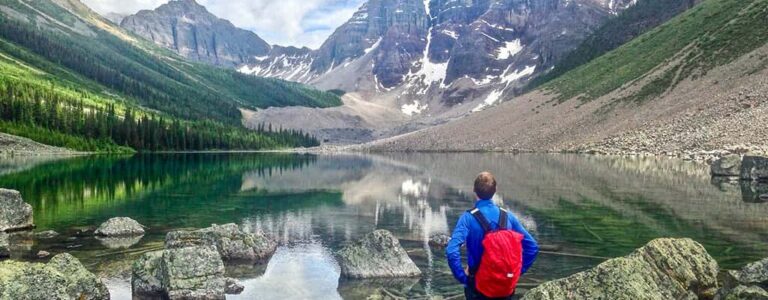 Wanderer an einem klaren Bergsee in Kanada vor schneebedeckten Gipfeln und Felswänden