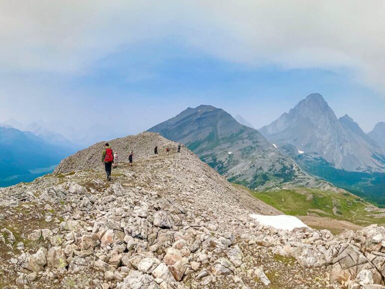 Wandergruppe auf einem felsigen Grat in Kanada mit weitem Blick auf Berge und Seen