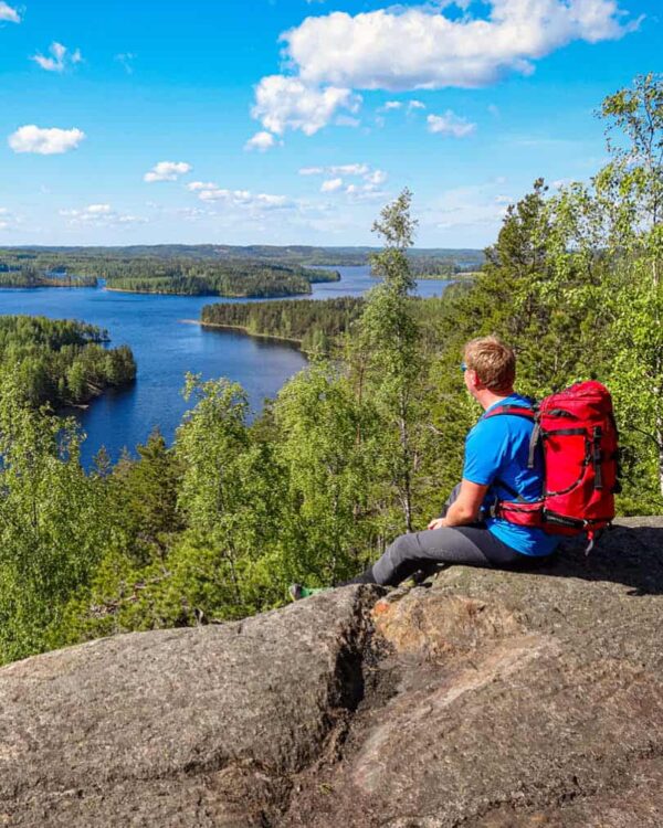 Ein Wanderer sitzt vor einem Ausblick in Finnland und schaut die Küste hinab.